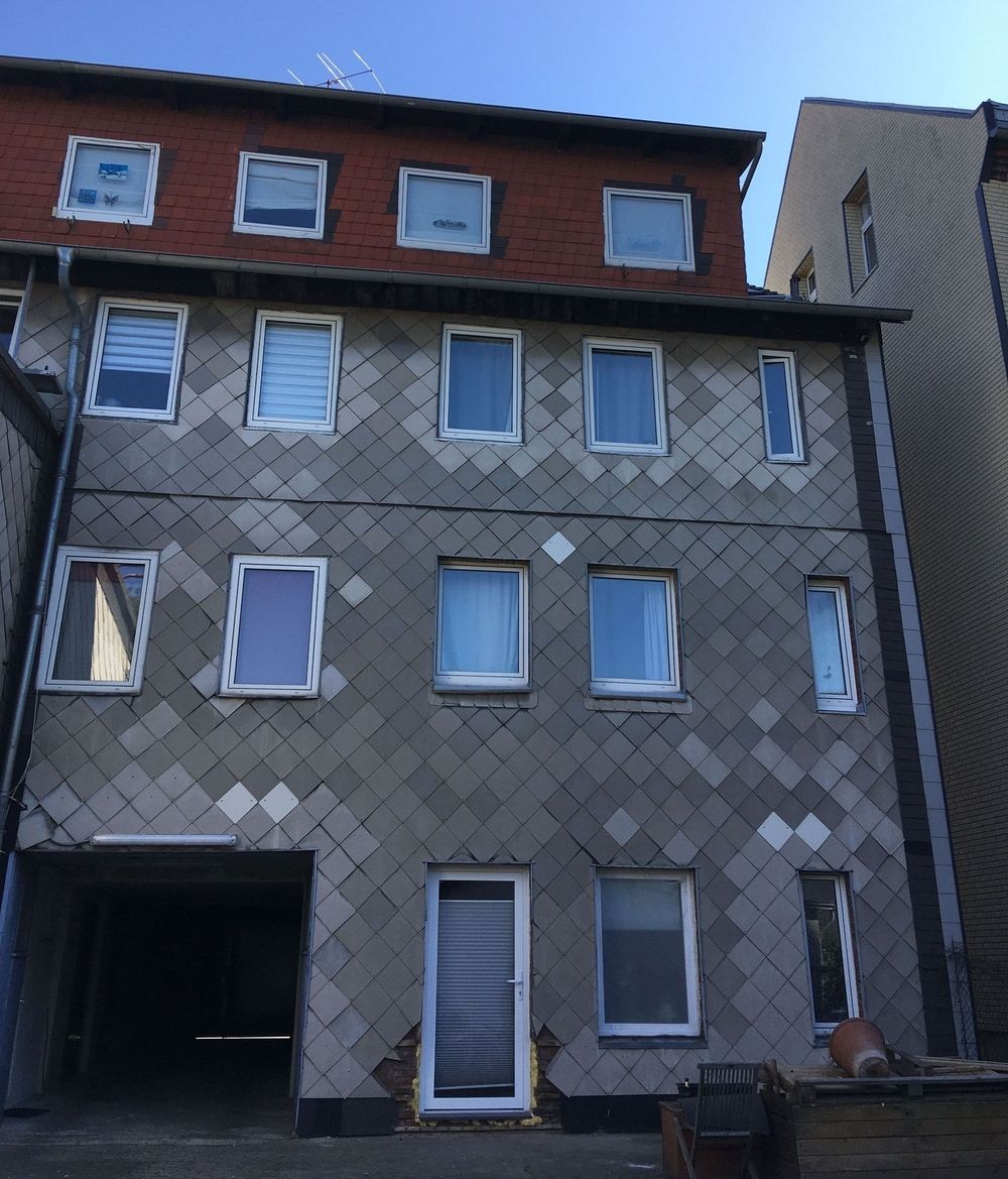 Dreistöckiges Gebäude mit einer strukturierten Schieferfassade mit verschiedenen Fenstertypen und -farben