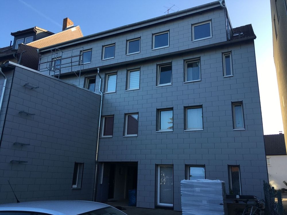 Ein modernes, graues, mehrstöckiges Gebäude mit verschiedenen Fenstermotiven, Gerüsten und Baumaterialien